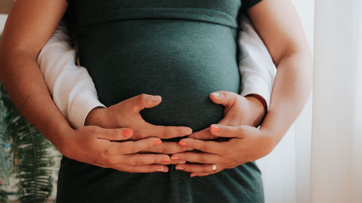 Two people's hands on a pregnant belly, symbolizing fertility.