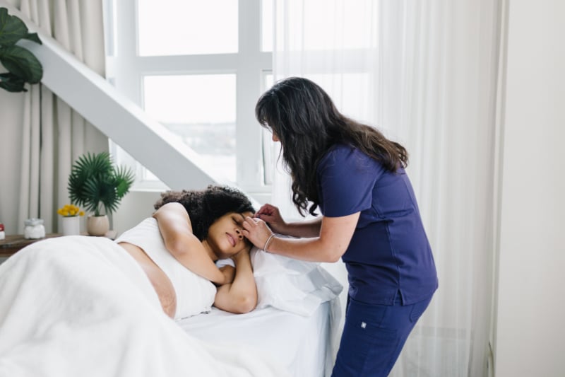 A healthcare professional checks on a patient resting in bed, focusing on pregnancy care.