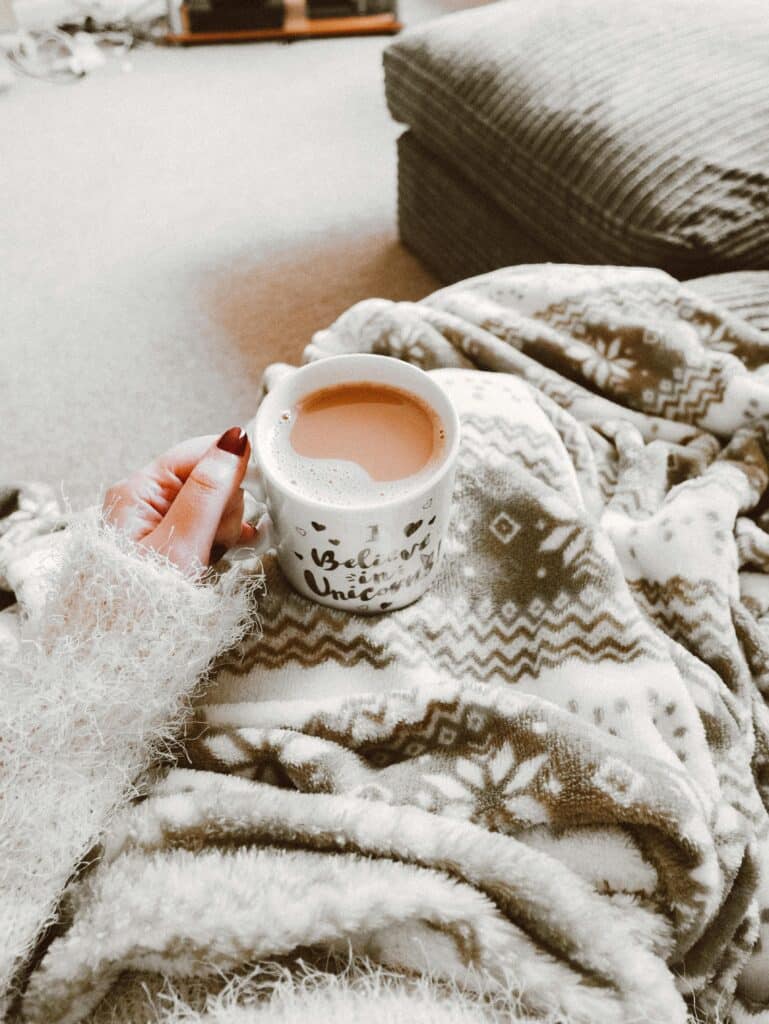 a person with a cup of tea sitting in a blanket