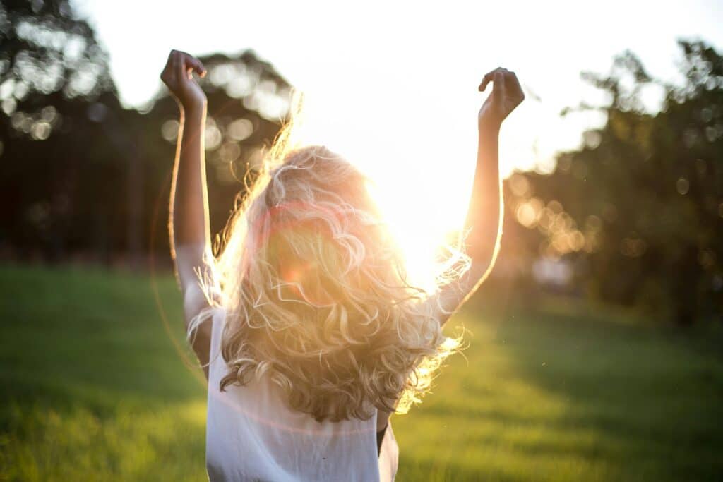 a person standing in a sunlit field, arms raised in a gesture of freedom and vitality, with sunlight streaming through their hair. This sense of well-being and energy reflects the benefits of acupuncture for breast health, as it helps relieve discomfort and supports overall emotional balance.