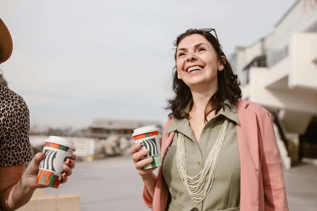 a woman outside smiling and drinking coffee with her friends.