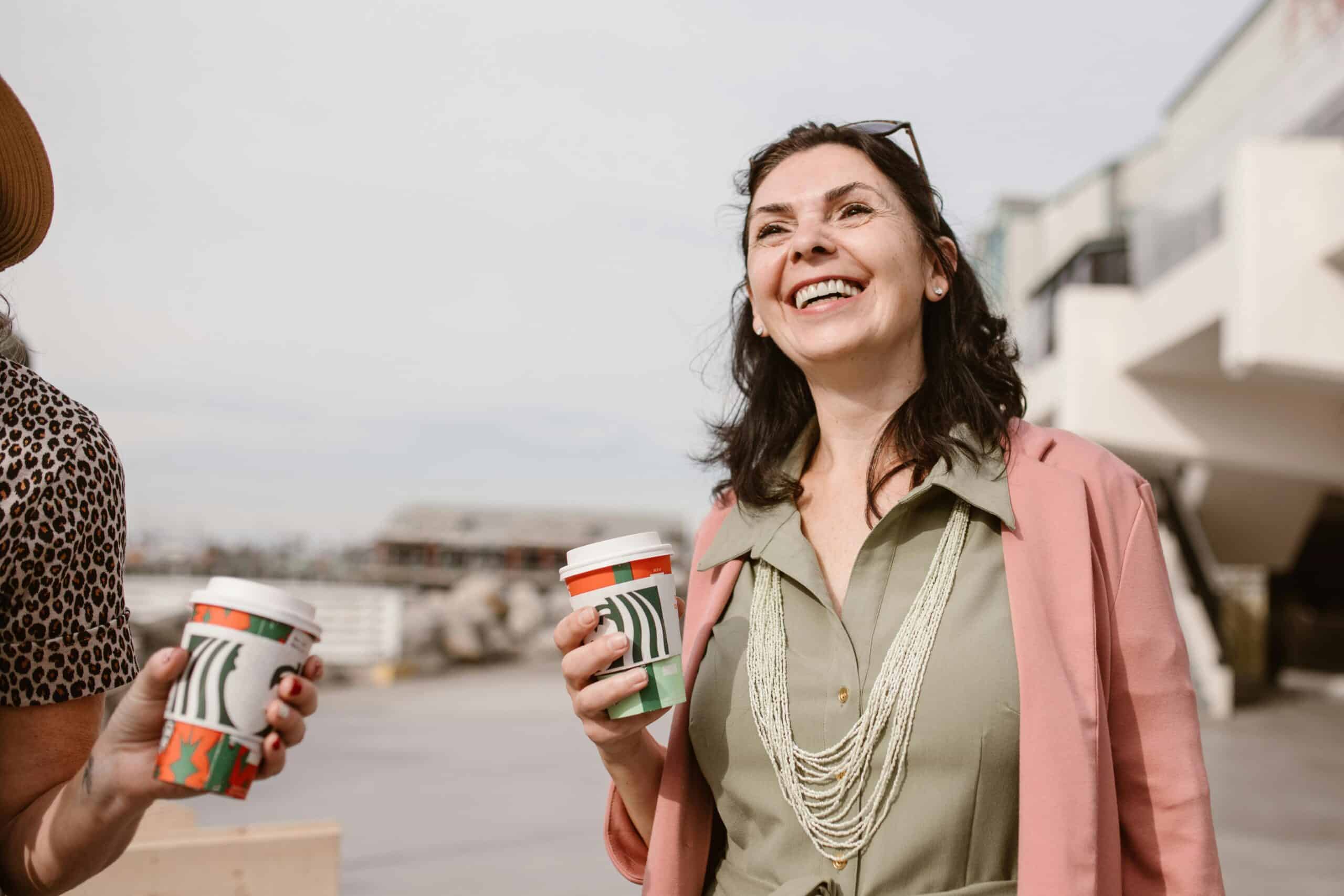 a woman outside smiling and drinking coffee with her friends.