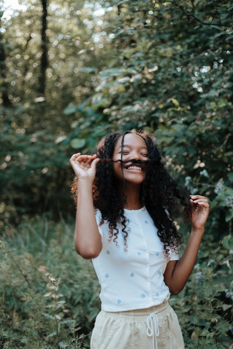 Playful woman smiling outdoors in nature, showing the emotional balance and joy that can come from tune-up acupuncture care.
