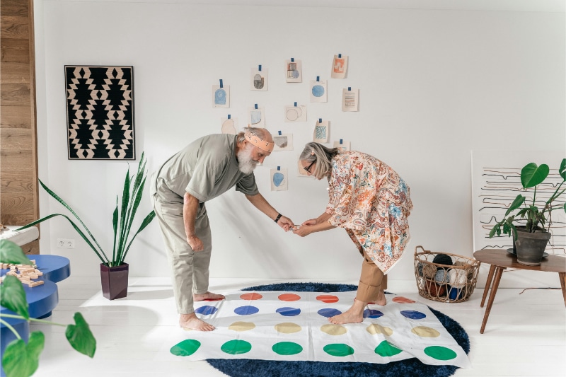 Elderly man and woman play a game of Twister in their living room.