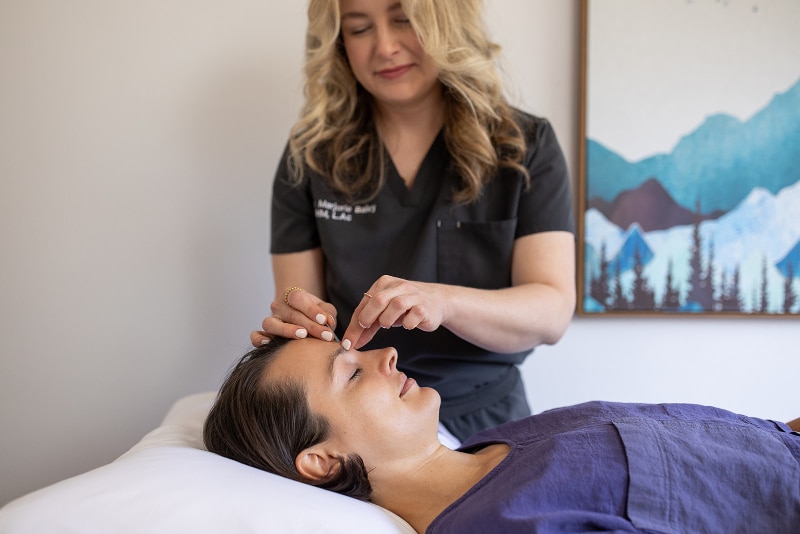Acupuncturist gently placing a needle on a relaxed patient's forehead during a treatment session in a peaceful clinic setting.
