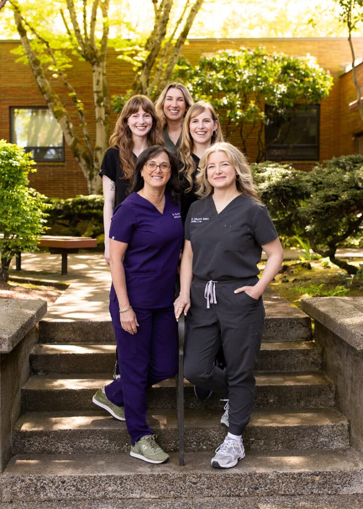 Five healthcare practitioners stand together on concrete stairs in a sunny outdoor setting with lush greenery. Their professional yet approachable presence reflects a clinic focused on holistic health and the principles of the chinese medicine clock.