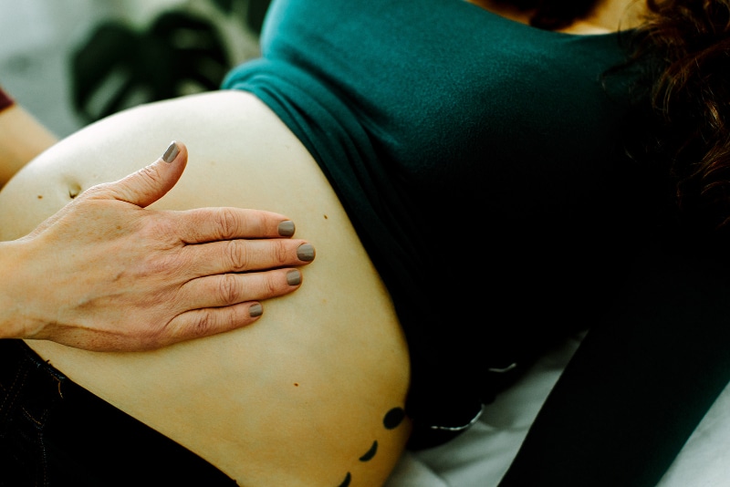 Hand resting gently on a pregnant belly during treatment, illustrating a calm and supportive environment for those searching pregnancy acupuncture near me for prenatal relief and comfort.