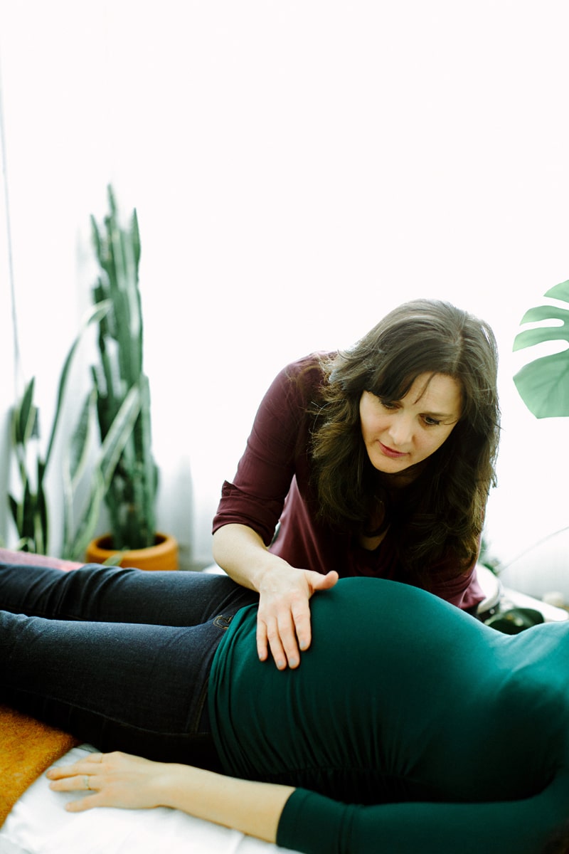 Practitioner assessing a pregnant patient’s belly in a peaceful clinic setting, representing the personalized care people expect when looking for pregnancy acupuncture near me in Portland.