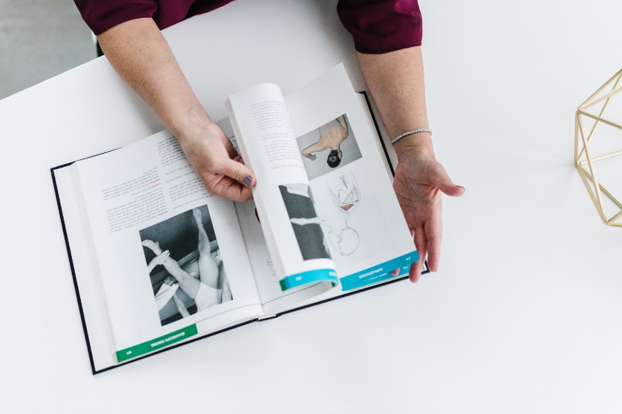 A practitioner flips through a clinical reference book, reviewing anatomy and treatment techniques. This reflects the thoughtful, evidence-based approach behind Acupuncture for PCOS Portland Oregon.