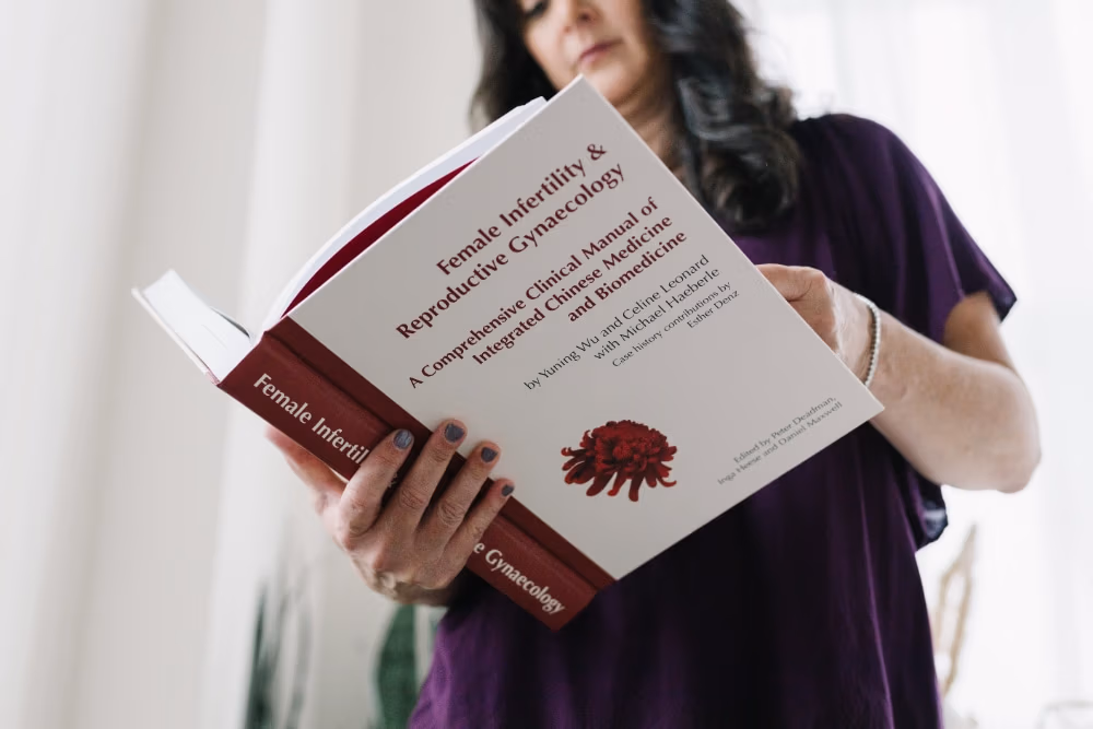 Portland Acupuncture practitioner reading a fertility and Chinese medicine textbook, reflecting research-backed care behind real fertility success stories and acupuncture support