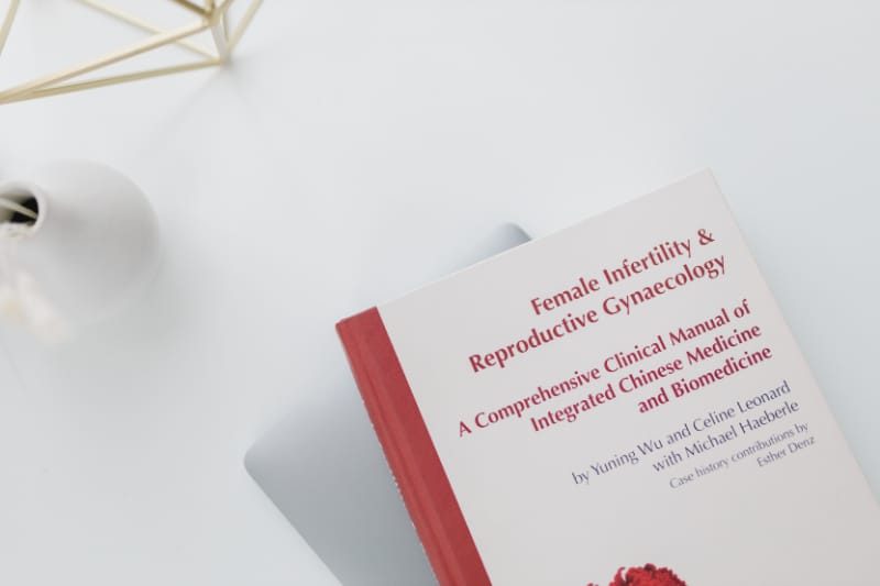 Book titled “Female Infertility & Reproductive Gynaecology” on a clean white surface, representing clinical knowledge behind fertility acupuncture and evidence-based care at a Portland acupuncture clinic.